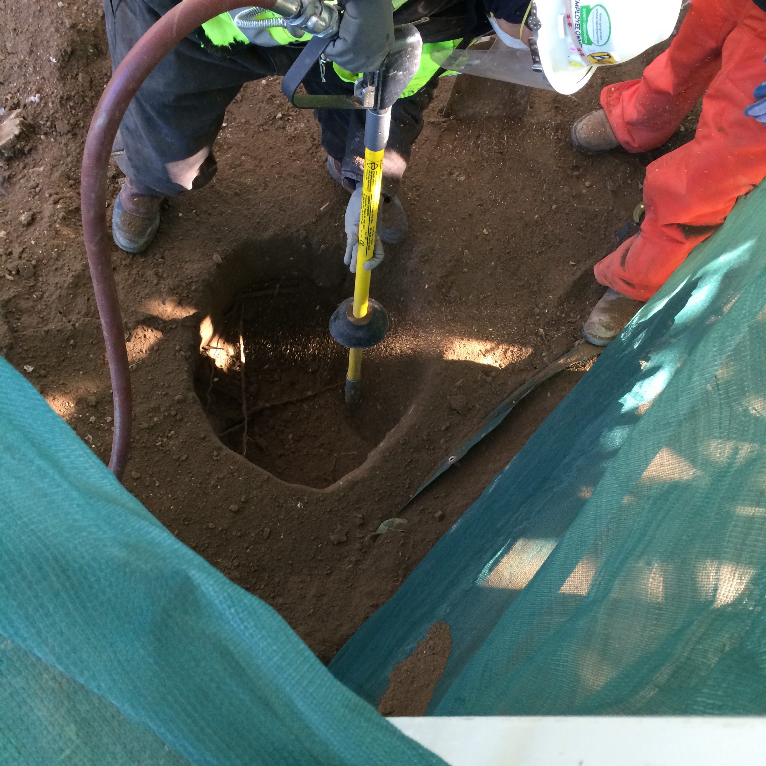Air-Spade operator in safety gear excavating tree roots at Austin construction site